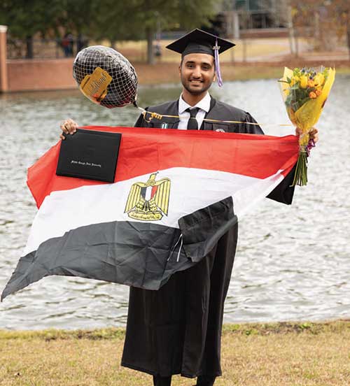 An international student in graduation cap and gown holding an Egyptian flag.